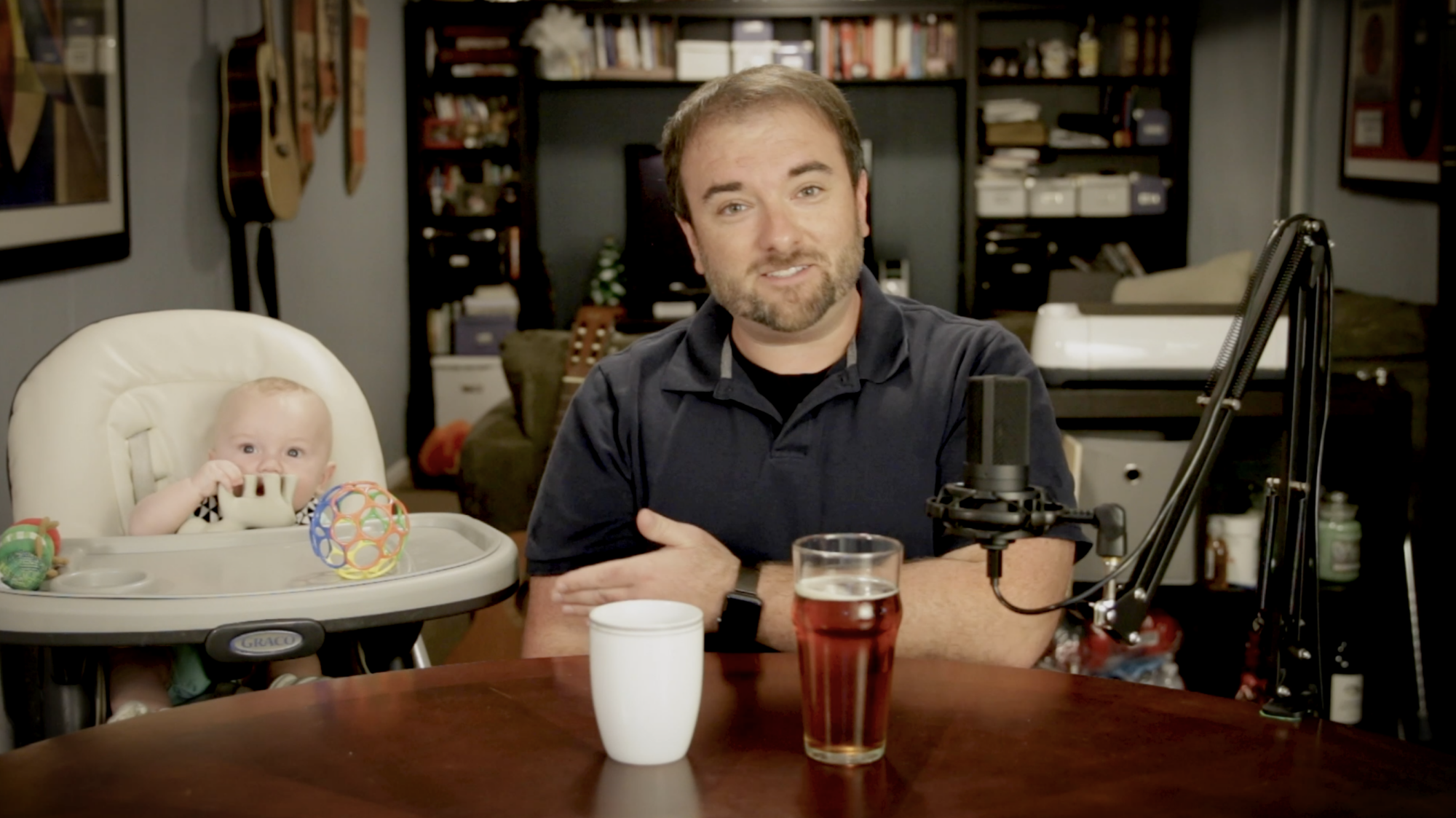 Chris sits with his son with a coffee and a beer. Neither are for the baby.