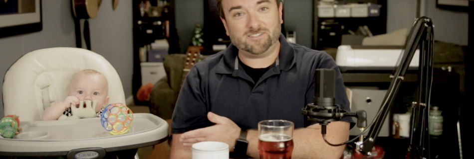 Chris sits with his son with a coffee and a beer. Neither are for the baby.